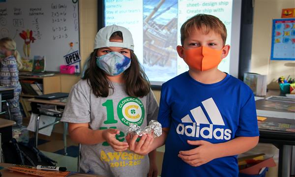 Students smile holding an aluminum boat